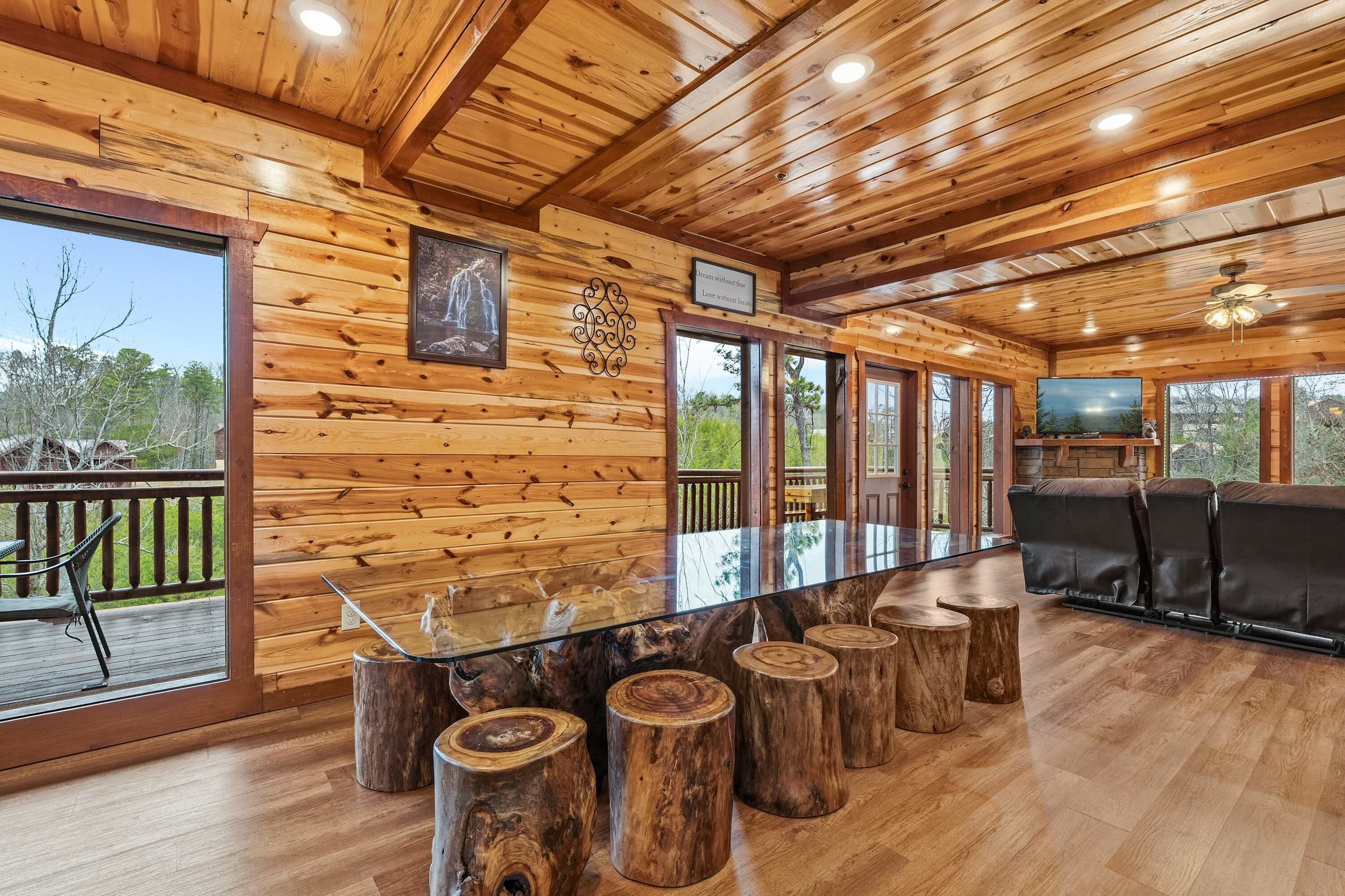 Un intérieur en bois avec une table à manger dont le plateau est en verre, entourée de tabourets en bois, un téléviseur et un coin salon avec un canapé.