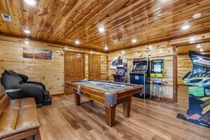 Ein Billardtisch in einem Raum mit Holzwänden und -decke, einer Couch und Spielautomaten.