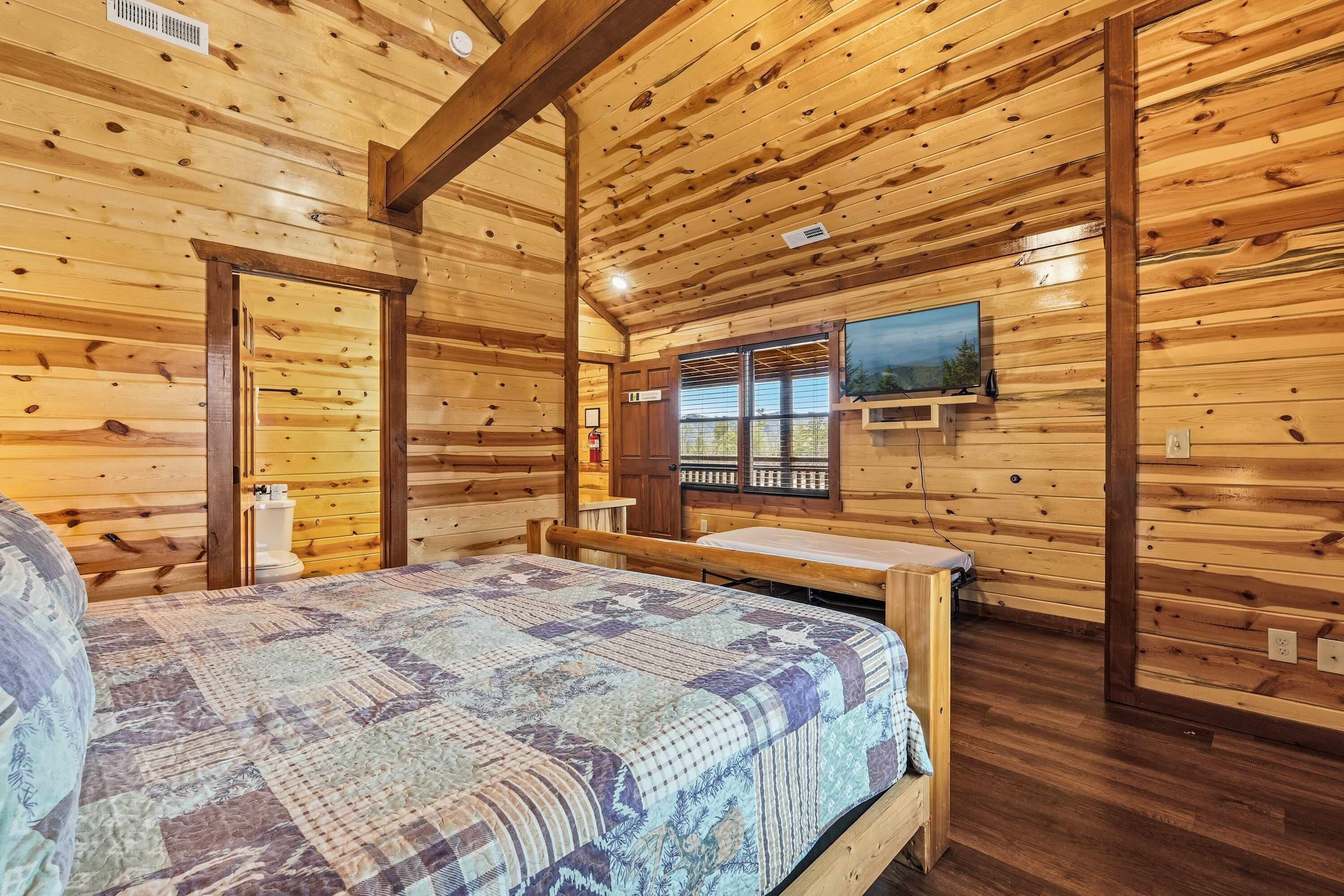 A wooden cabin interior with a bed, a window with a view, and a mounted television.