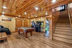 Ein Holzinterieur mit Billardtisch, Spielautomaten und einer Treppe.