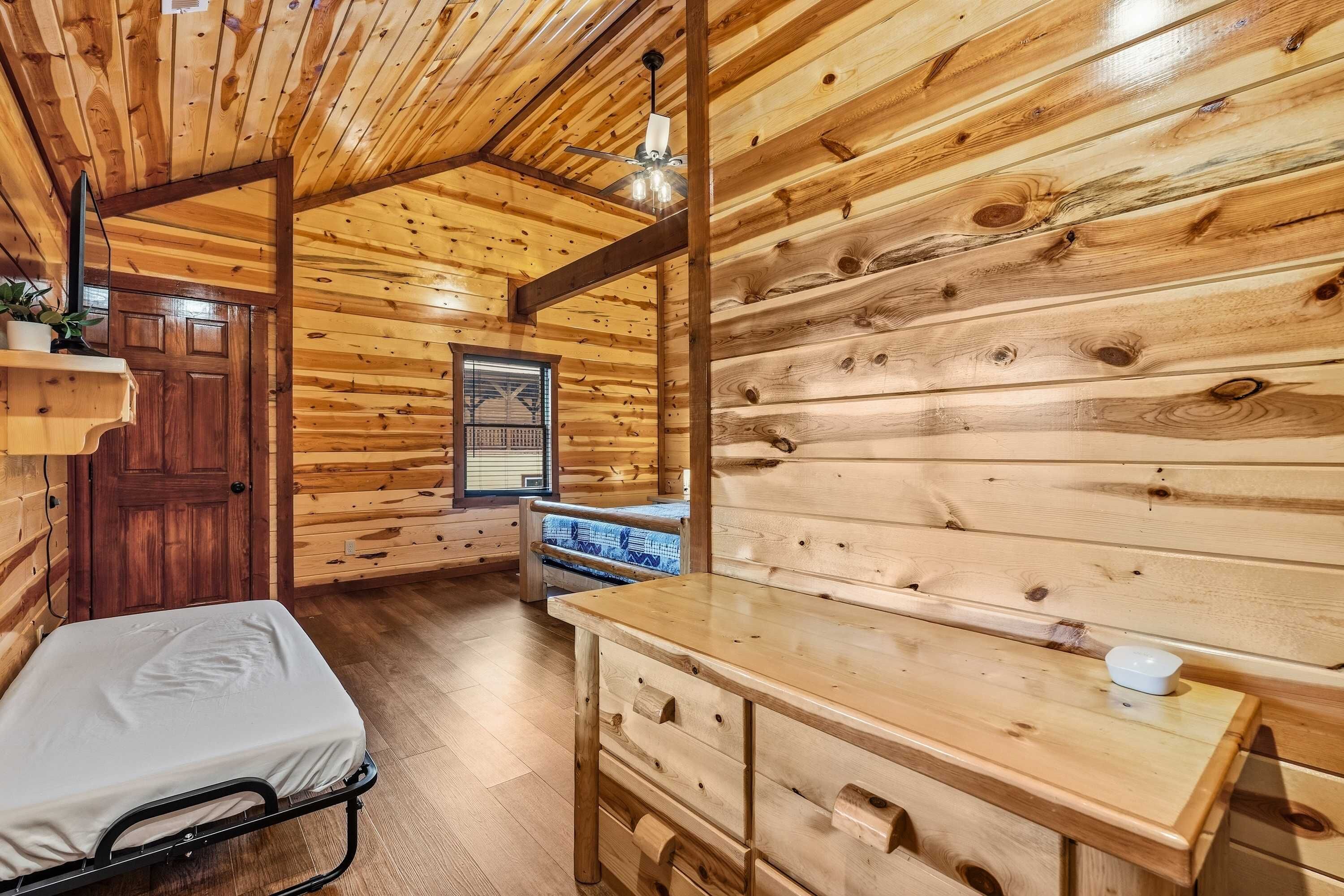 A cabin interior with a bed, wooden dresser, and a window.