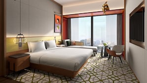 Ein Hotelzimmer mit einem großen Bett, einem Schreibtisch, einem Stuhl, einem kleinen Tisch und Blick auf die Stadt.