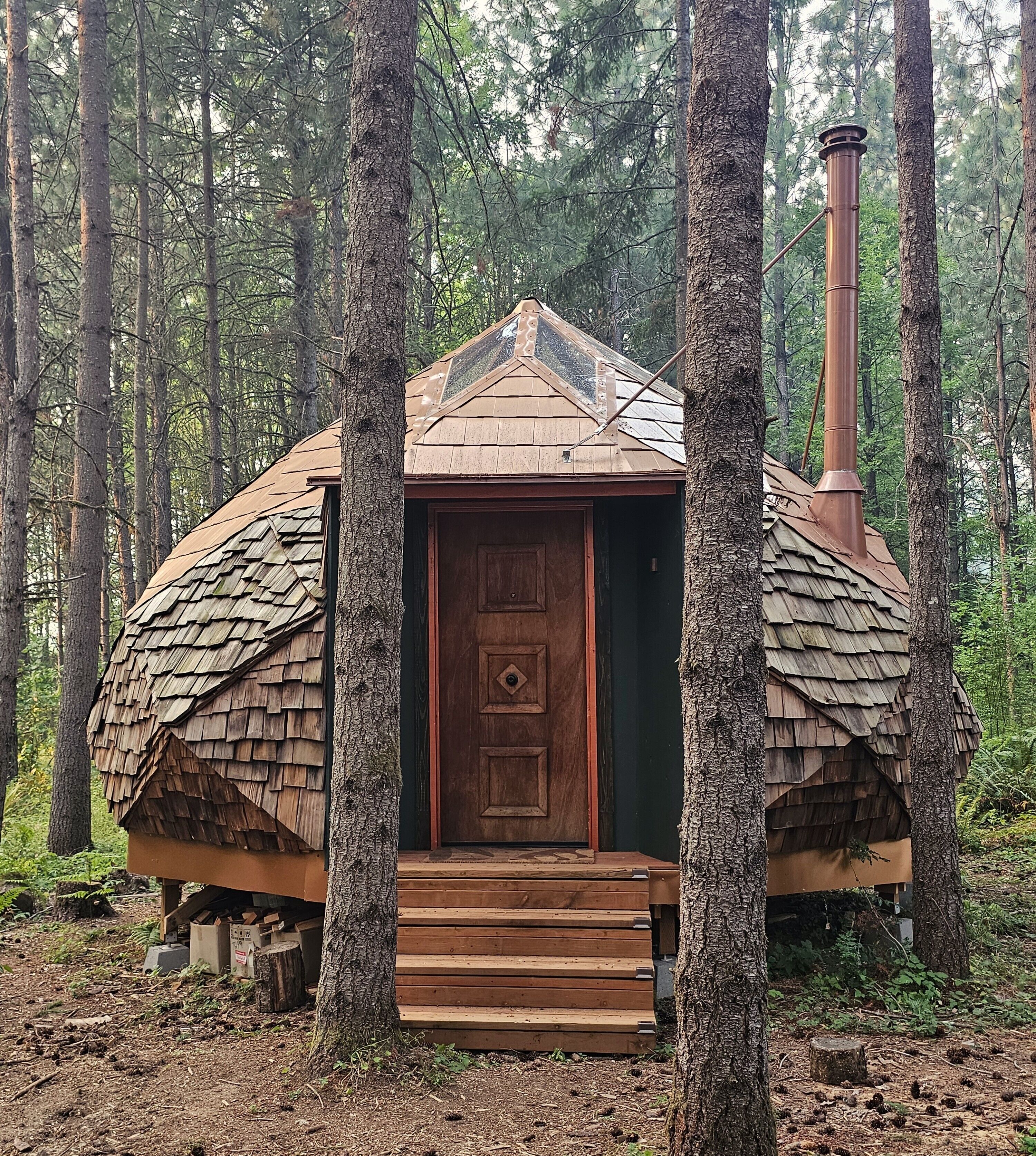 Maalaishenkinen mökki, jossa on puinen ovi ja jonka ympärillä kasvaa puita.