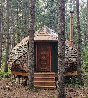 Eine rustikale Holzhütte mit einer Holztür, umgeben von Bäumen.