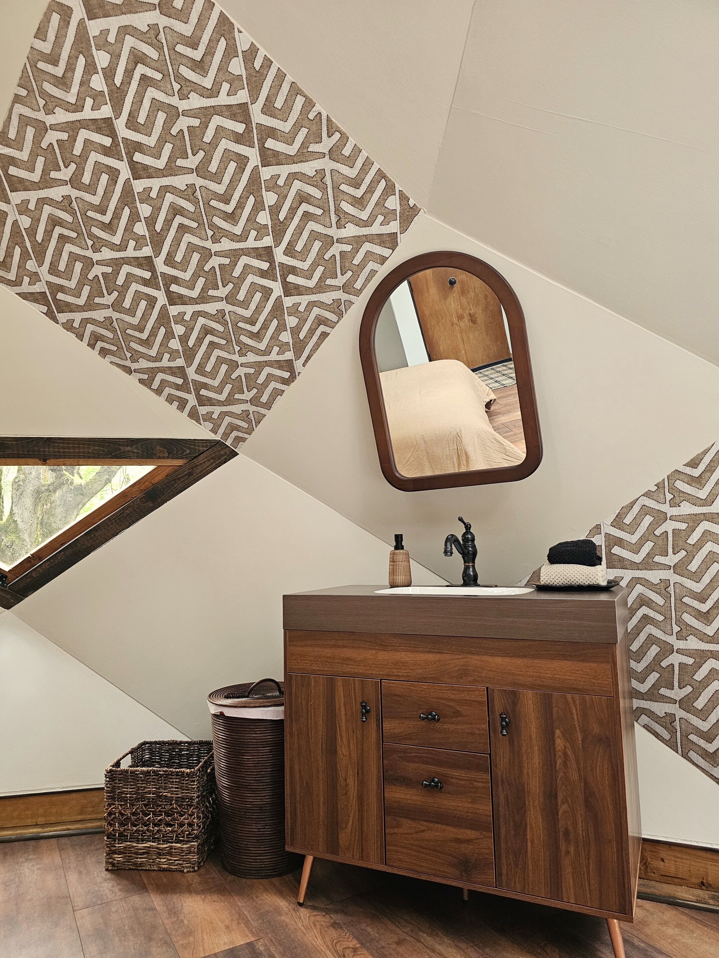 Baño con tocador de madera, espejo y azulejos con diseño.