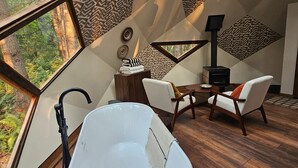 Interior moderno com uma banheira grande, soalho de madeira e vista para uma floresta através de uma janela geométrica.