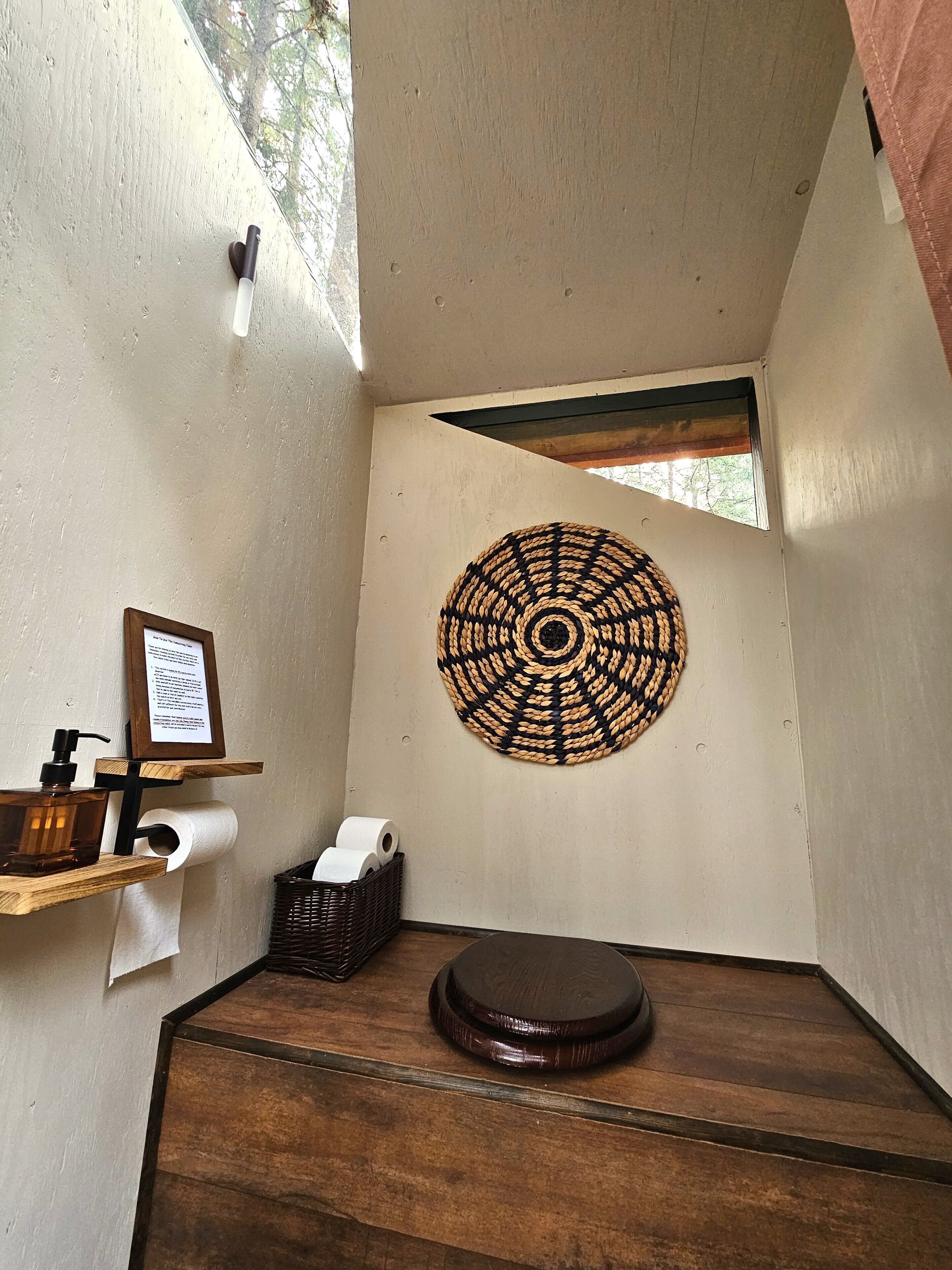 Um banheiro pequeno e fechado com piso de madeira, vaso sanitário, dosador de sabonete líquido, suporte para toalhas de papel e um detalhe decorativo na parede feito de tecido.