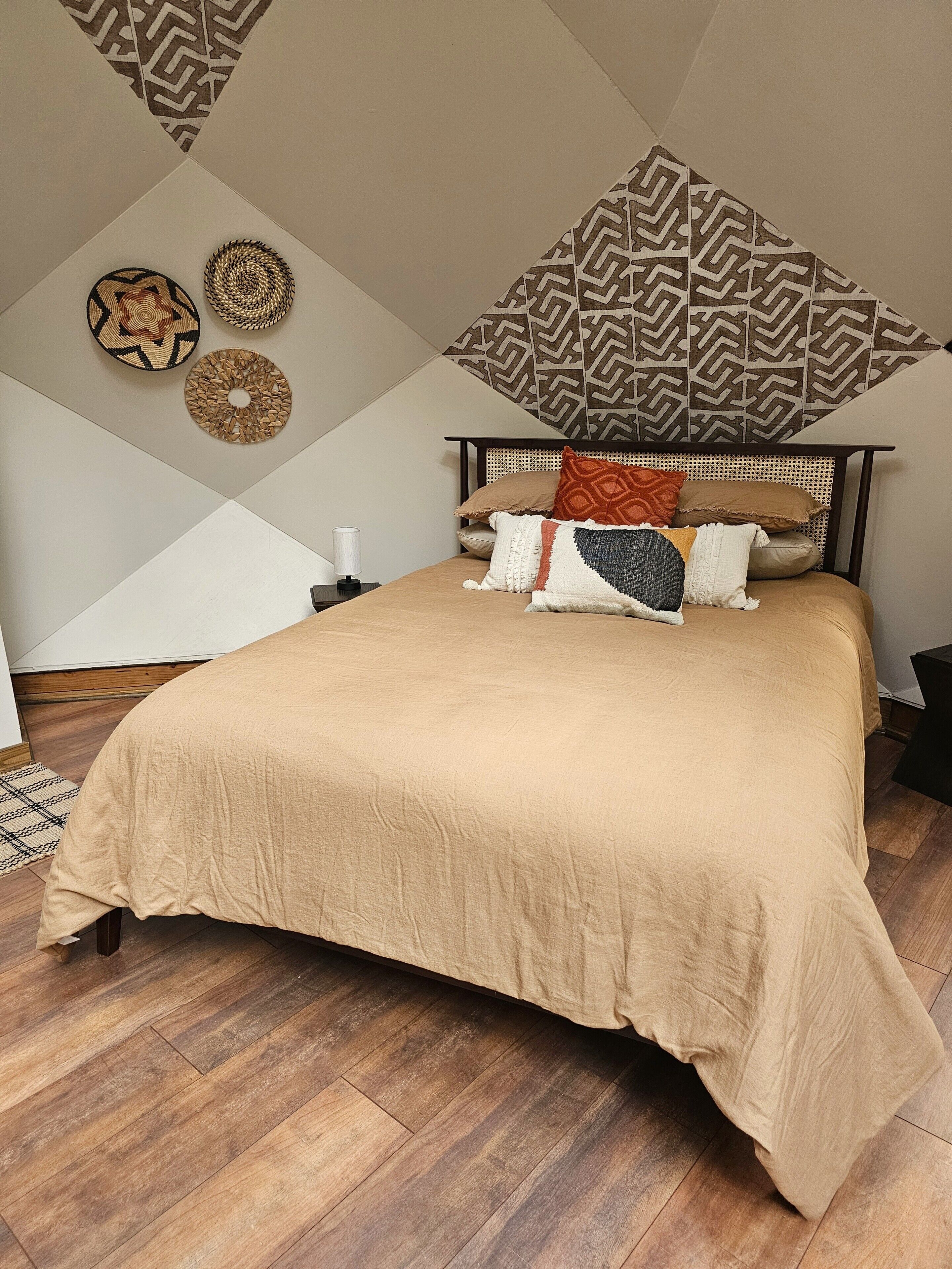 A bedroom with a large bed, a headboard, and a geometric-patterned wall hanging.