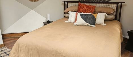 A bedroom with a large bed, a headboard, and a geometric-patterned wall hanging.