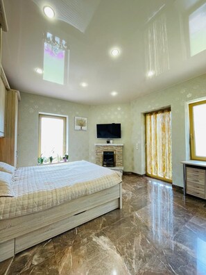 Ein Schlafzimmer mit Bett, Fernseher, Kamin und großem Fenster.