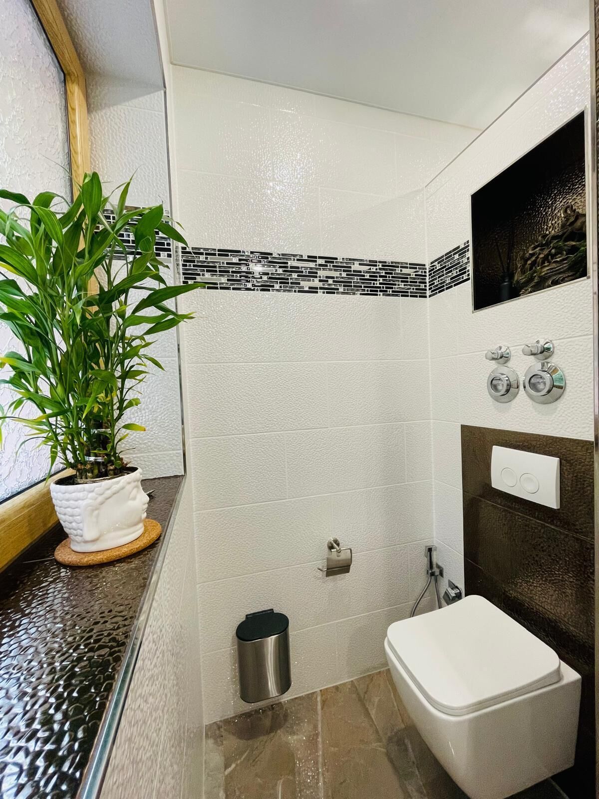 A bathroom with a white toilet, a sink with a faucet, a trash can, and a potted plant.
