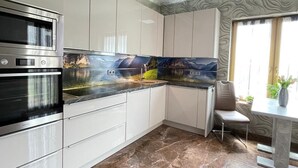 Ett modernt kök med vita skåp, en ugn i rostfritt stål och ett golv av marmor.