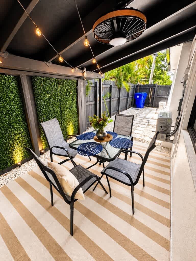 An outdoor patio with a table and chairs, surrounded by a green wall and a striped floor.