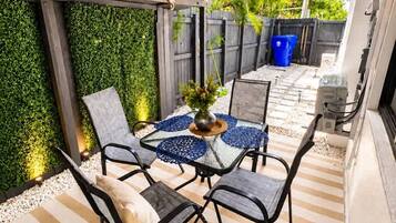 An outdoor patio with a table and chairs, surrounded by a green wall and a striped floor.