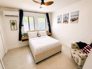 A bedroom with a bed, a nightstand, a window with curtains, and a wall with three framed pictures. - Cozy 1BR Near Brickell (Miami)