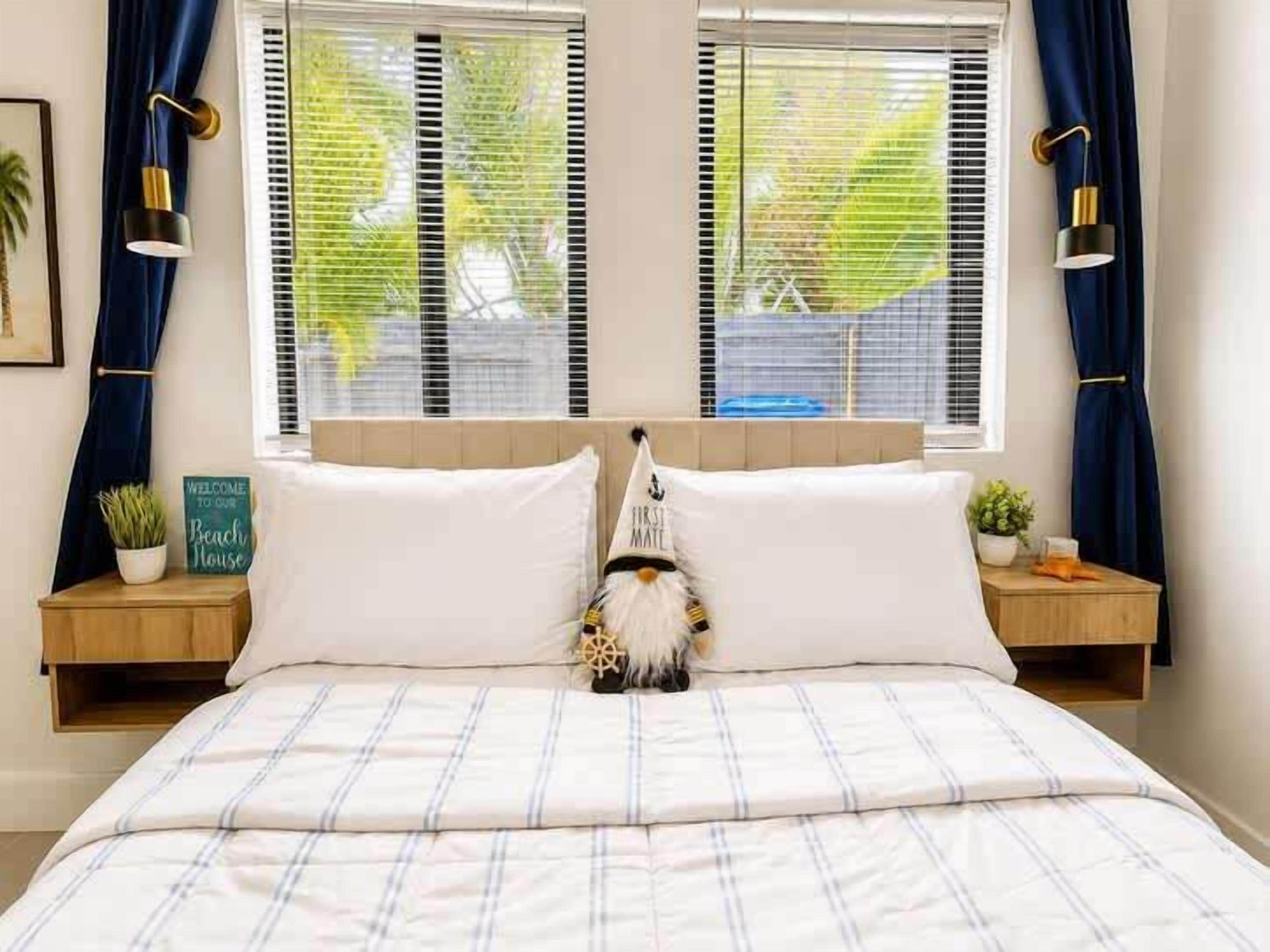 A bedroom with a bed, two bedside tables, a nightstand, a wall-mounted lamp, and a window with curtains.