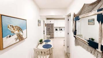 A hallway leading to a dining area with a table and chairs, a painting on the wall, and a kitchen in the background.