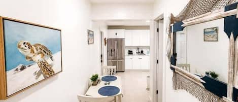 Un pasillo que conduce a un comedor con una mesa y sillas, un cuadro en la pared y una cocina al fondo.
