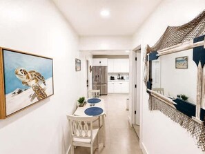 A hallway leading to a dining area with a table and chairs, a painting on the wall, and a kitchen in the background. - Cozy 1BR Near Brickell (Miami)