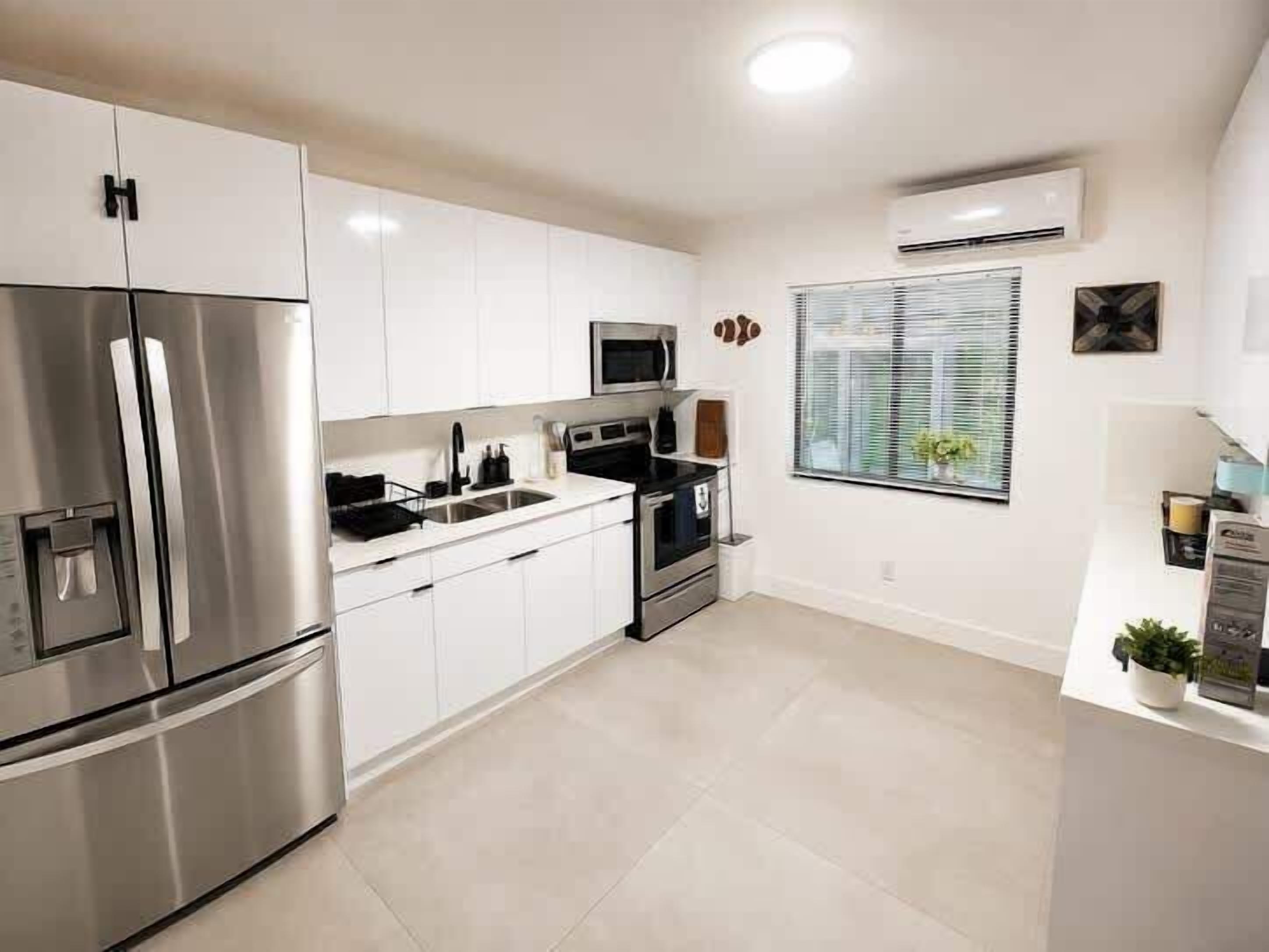 A modern kitchen with stainless steel appliances, white cabinetry, and a window with blinds.