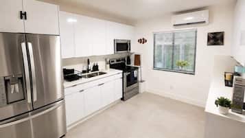 A modern kitchen with stainless steel appliances, white cabinetry, and a window with blinds.