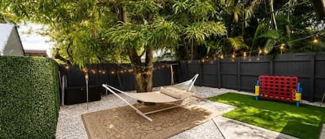 Un patio trasero con una hamaca, un pequeño espacio de juegos y césped artificial verde.