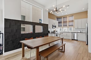 Eine moderne Küche mit schwarzem Fliesenspiegel, weißen Schränken, einem Holztisch und einem zeitgemäßen Kronleuchter.