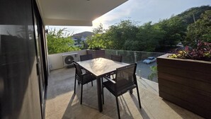 Ein Balkon mit Tisch und Stühlen, einer Klimaanlage und Blick auf die Straße sowie auf Grünflächen.