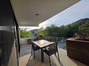 A balcony with a table and chairs, an air conditioning unit, and a view of the street and greenery. - Estudio a pasos de playa Santa Cruz (Bahía de Santa Cruz Huatulco)