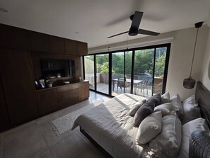 Ein Schlafzimmer mit einem Bett, einem Fernseher, einem Deckenventilator und einem großen Fenster.