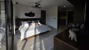 Ein modernes Schlafzimmer mit einem großen Bett, einem Deckenventilator und Blick auf den angrenzenden Wohnbereich.