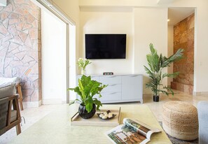 A modern living room with a stone wall, a flat-screen TV mounted above a grey cabinet, a potted plant, and a woven ottoman. -     Luxury 3 Bedroom Penthouse Steps from the Beach (Puerto Vallarta)