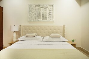 A bedroom with a tufted headboard, a bed with white linens, a bedside lamp, and a small plant on a nightstand. -     Luxury 3 Bedroom Penthouse Steps from the Beach (Puerto Vallarta)