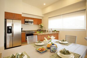 A modern kitchen with stainless steel appliances, a dining table set with plates and a vase of flowers. -     Luxury 3 Bedroom Penthouse Steps from the Beach (Puerto Vallarta)