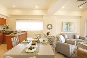 Cozinha moderna com área de refeições, sala de estar com sofá e mesa posta para uma refeição.
