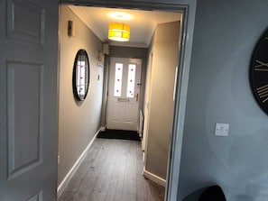En hall med en dörr i slutet, en spegel som hänger på väggen och en taklampa.