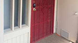 A red door with a keypad lock, a welcome sign above it, and a small vent on the wall.