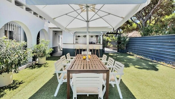 Une terrasse avec une table et des chaises, un grand parasol et un espace barbecue.