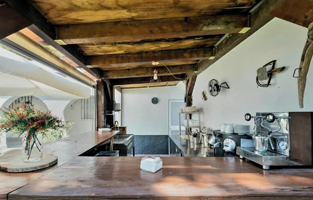 A rustic kitchen with exposed wooden beams, a large window, and vintage espresso machines.