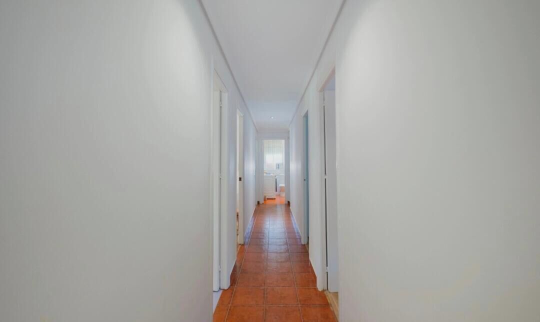 Un pasillo con paredes blancas y piso de baldosas que conduce a una puerta al final.