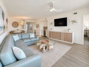 Ein modernes Wohnzimmer mit einem Ecksofa, einem Glastisch und einem flachbildfernseher, der an der Wand befestigt ist.