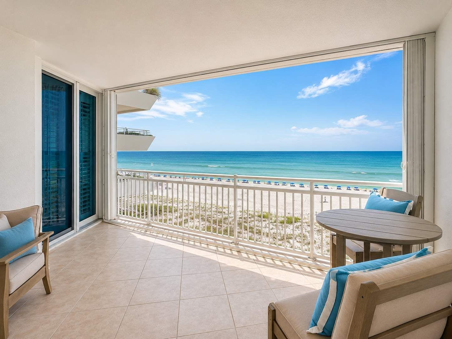 A balcony with a view of the beach, a round table, and a sofa.