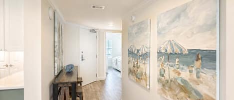 Un couloir au plancher de bois, une table à manger avec des chaises et deux grandes peintures accrochées aux murs.