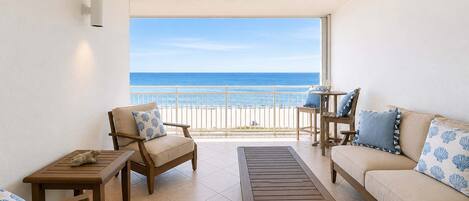 A balcony with a view of the beach, furnished with a sofa, chairs, and a table.