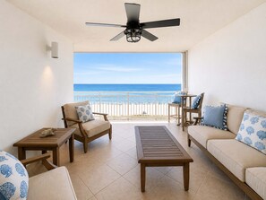 Ein Balkon mit Blick auf den Strand, möbliert mit einer Couch, Sesseln und einem Tisch.