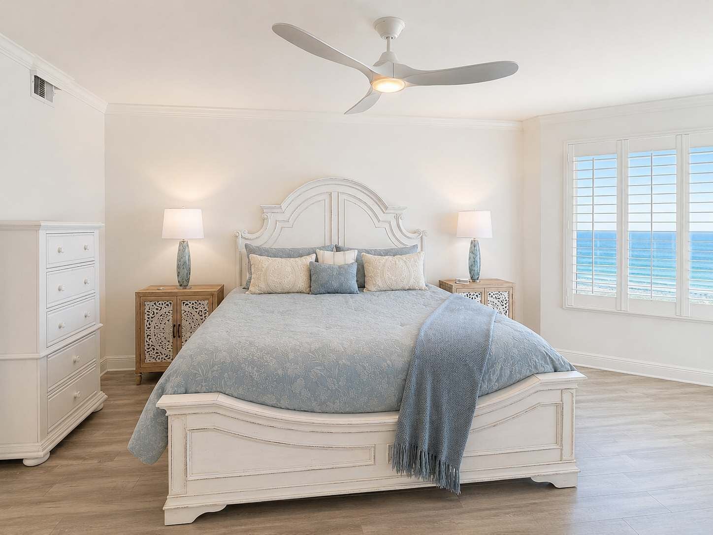 A bedroom with a large bed, two bedside tables, a ceiling fan, and a window with a view.