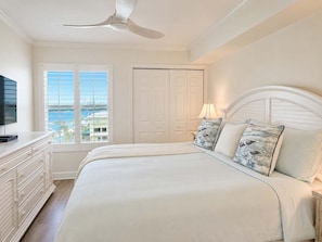 Ein Schlafzimmer mit einem Bett, einer Kommode, einem Deckenventilator, einem Fenster mit Jalousien und Blick ins Freie.