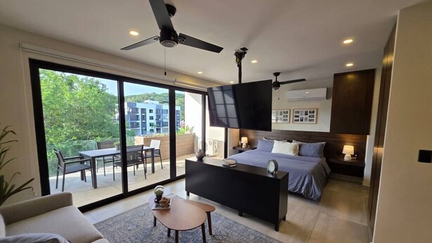 A modern hotel room with a bed, a sofa, a coffee table, and a TV. - Departamento una recámara en Santa Cruz (Bahía de Santa Cruz Huatulco)