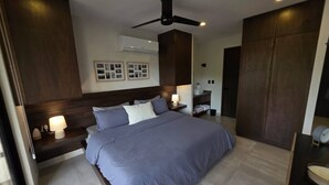 A modern bedroom with a large bed, a ceiling fan, and a nightstand with a lamp. - Departamento una recámara en Santa Cruz (Bahía de Santa Cruz Huatulco)