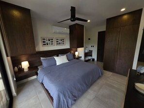 Ein modernes Schlafzimmer mit einem großen Bett, einem Deckenventilator und einem Nachttisch mit Lampe.